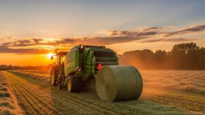 green tractor pulling a hay baler in a field
