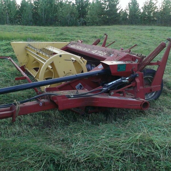 A red and yellow New Holland hay conditioner sits in a green field, ready to mow and process forage.